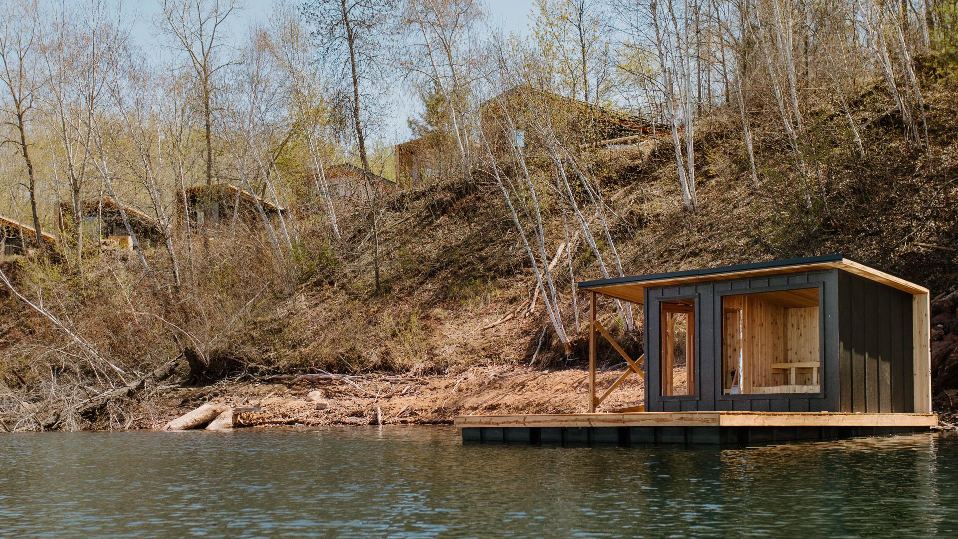 Floating wooden sauna anchored on a calm misty lake at dawn with ladder into water